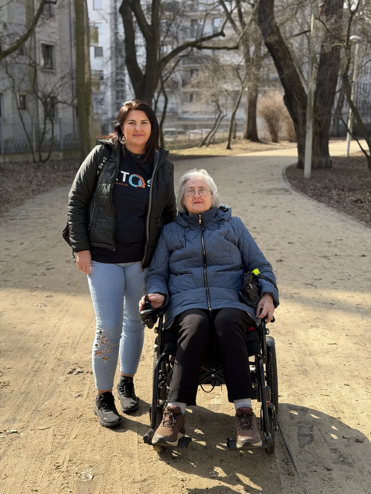 Dwie osoby idące trzymając się za ręce, jedna na wózku